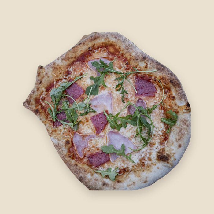 Frisch gebackene Pizza mit Rucola, Schinken und Salami, von oben