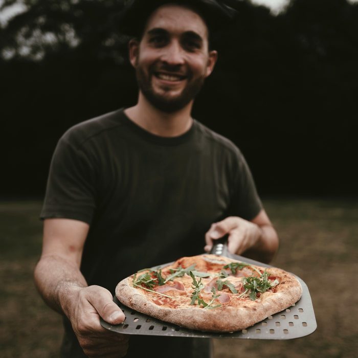 Silas reicht eine frisch gebackene Pizza mit Rucola auf dem Pizzaschieber weiter